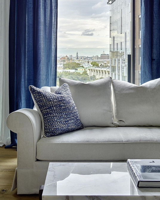 Простора вітальня з великим білим диваном та панорамними вікнами.