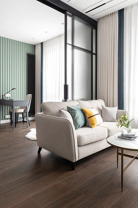 Білий диван з текстильною оббивкою, великою кількістю подушок та пледом у вітальні.