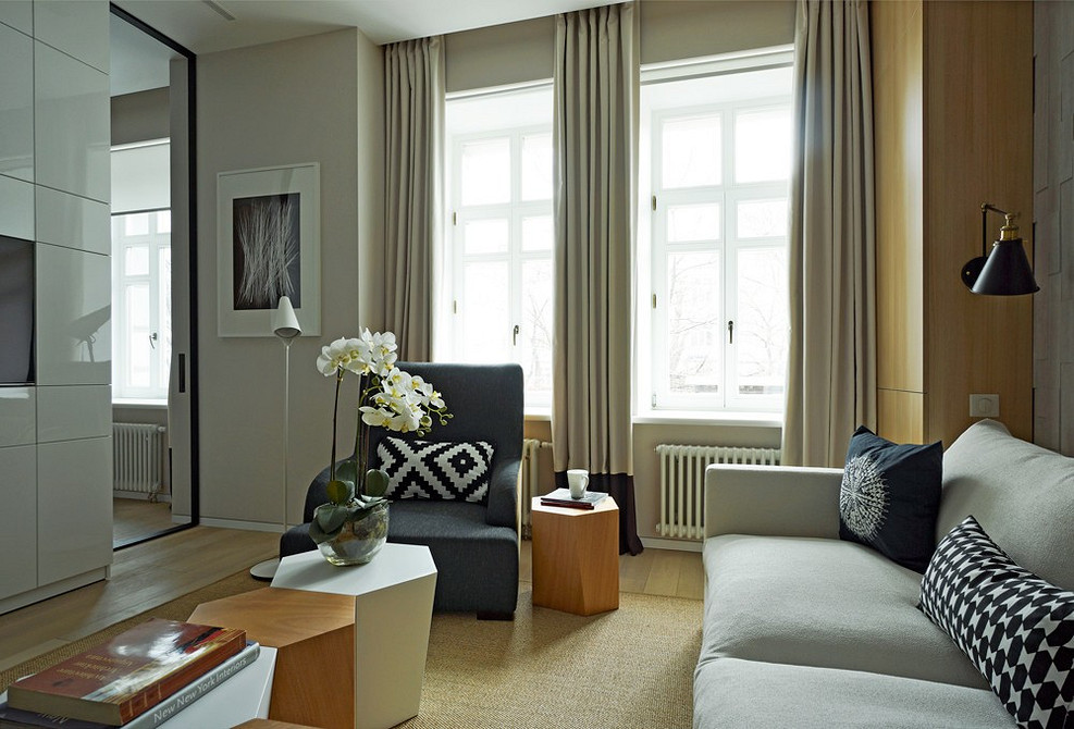 Білий диван в інтер'єрі вітальні з декоративними подушками та килимом, світлі меблі.