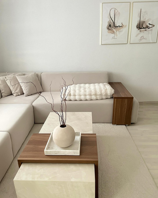 Бежевий диван з дерев'яними ніжками в інтер'єрі з акцентними синіми подушками та картиною.