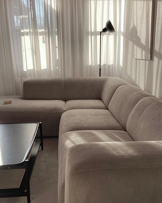 Сучасний бежевий диван з дерев'яними ніжками на фоні світлої стіни