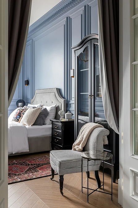 Стильна спальня з великим сірим ліжком, декоративними подушками та приліжковими тумбочками.