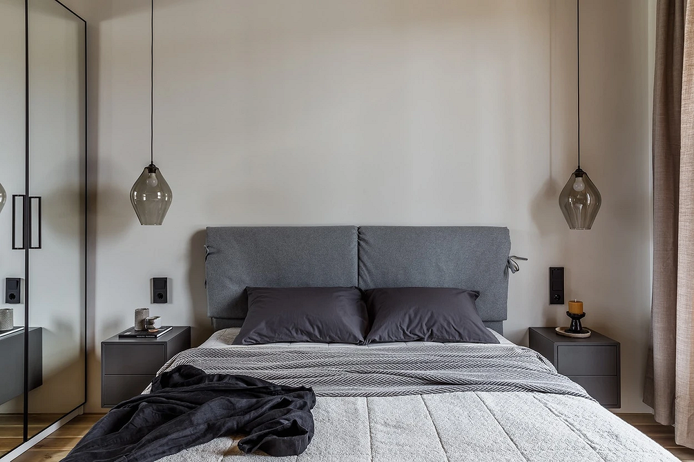Сіре ліжко з м'яким узголів'ям у спальні з нейтральними відтінками та декоративними подушками.