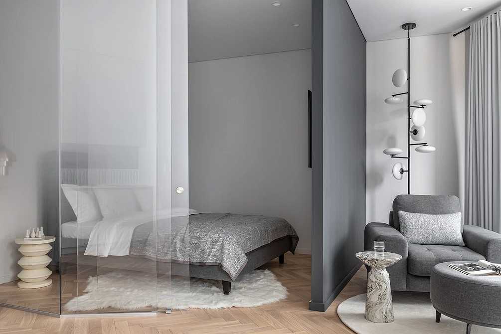 Сучасний дизайн спальні з сірим ліжком і мінімалістичним декором на стіні.