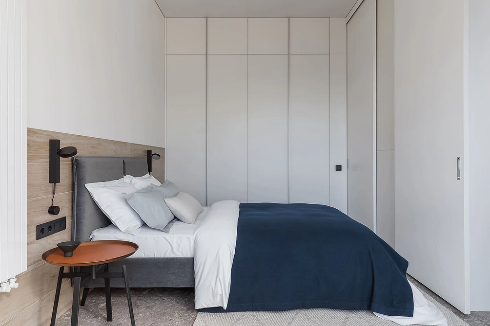 Сучасний дизайн спальні з сірим ліжком, великим дзеркалом та м'яким килимом.