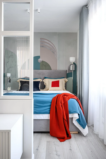 Затишна спальня з сірим ліжком, декоративними подушками та теплим освітленням.