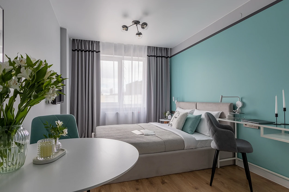 Стильна спальня з сірим ліжком, прикрашена рослинами та художніми елементами.