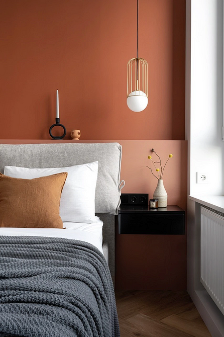 Світла спальня з сірим ліжком, прикрашена кімнатними рослинами та дерев'яними елементами.