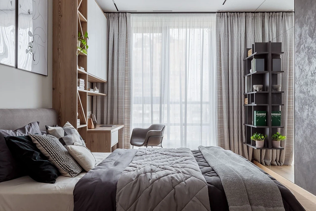 Стильна спальня з сірим ліжком, дерев'яною підлогою та сучасними світильниками.