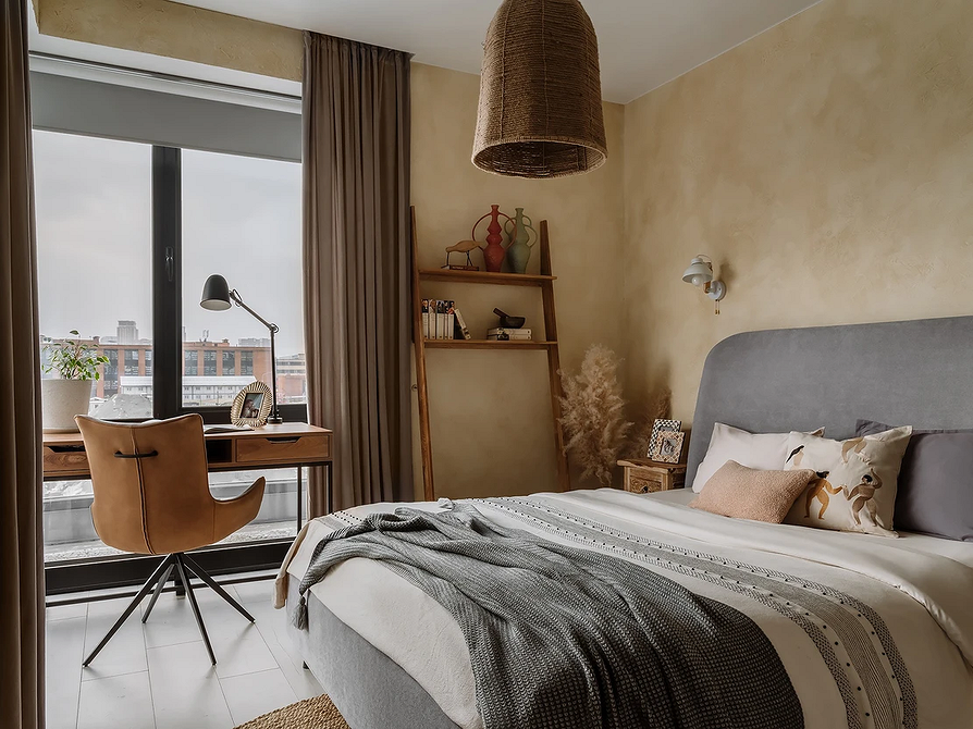 Інтер'єр спальні з сірим ліжком та постільною білизною в світлих тонах.