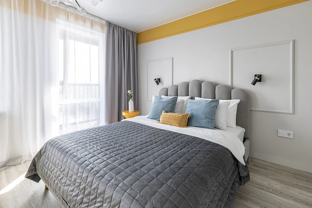 Елегантна спальня з сірим ліжком, текстилем в тон та акцентним освітленням.