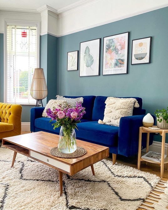 Затишна вітальня з синім диваном, пледом та декоративними подушками на дивані.