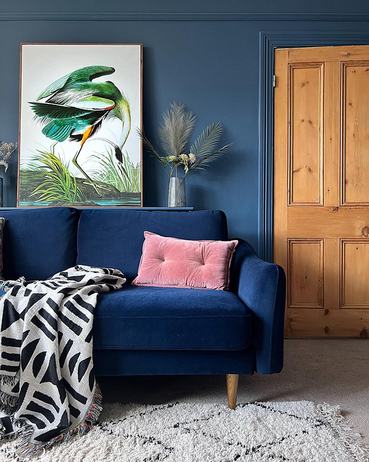 Вітальня з синім диваном, картинами на стінах та декоративними подушками.