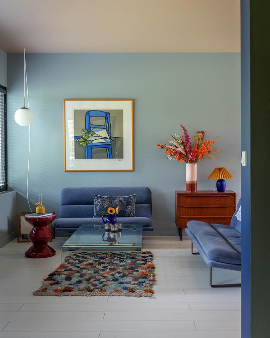 Інтер'єр з синім кутовим диваном, килимом з геометричним візерунком та рослинами.