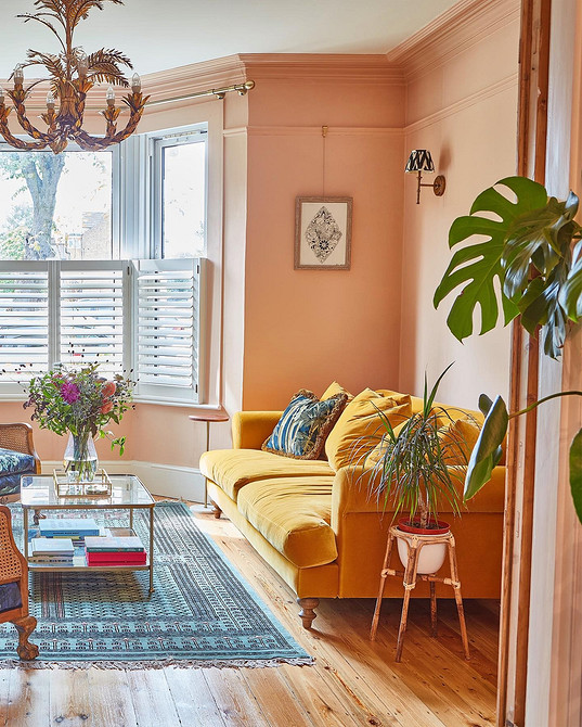 Жовтий диван з подушками різних кольорів у вітальні з рослинами та книжковою полицею.