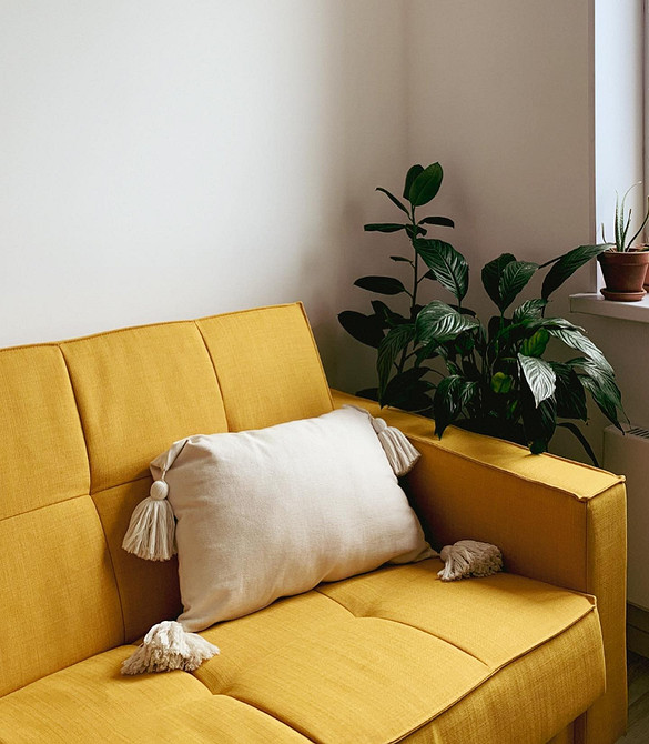 Жовтий диван в вітальні з великими вікнами, що забезпечують природне освітлення простору.