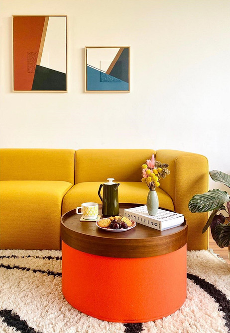 Жовтий кутовий диван в інтер'єрі вітальні з великими вікнами та рослинами