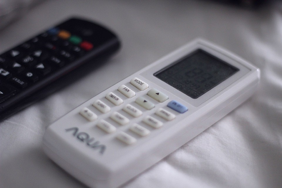 Керування кліматом Близьке зображення руки, що тримає пульт дистанційного керування кондиціонером, обираючи функцію.