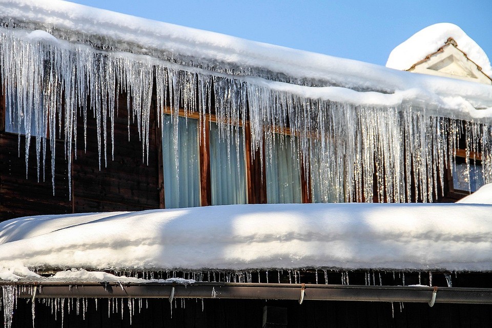 Безпечне збивання бурульок Ілюстрація: Людина збиває бурульки з даху за допомогою довгої жердини.